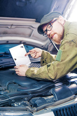 Mechanic Leaning on Car Pointing at Laptop