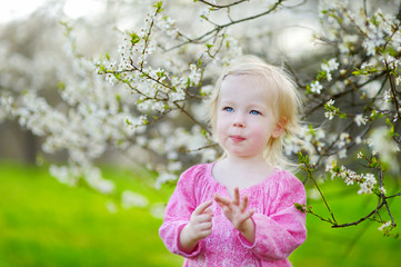 Adorable toddler girl in blooming cherry garden