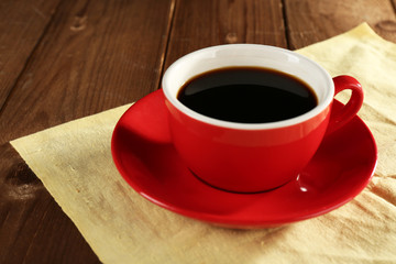 Cup of coffee on color napkin on wooden table background