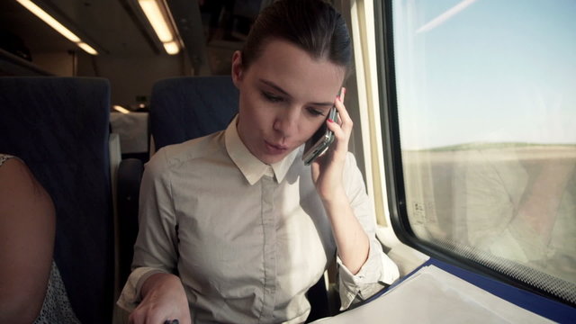 Businesswoman talking on cellphone and reading documents on a tr