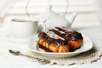 Tasty eclairs and cup of tea on wooden table