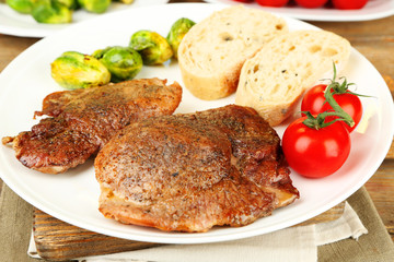 Roasted meat and vegetables on plate, on wooden table