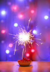 Tasty cake with sparkler on shiny background