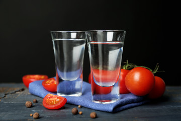 Glasses of ouzo and tomatoes on wooden table, on grey