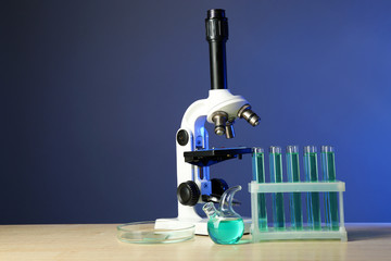 Microscope and test tubes on table, on color background