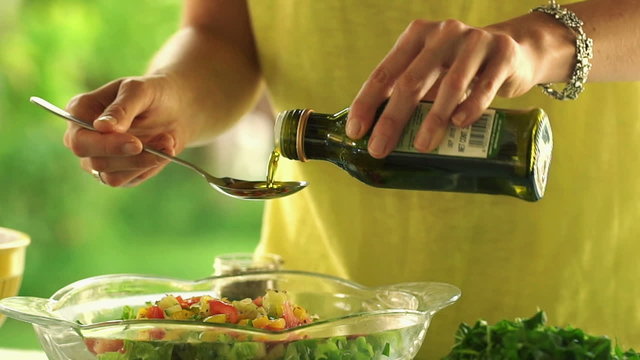 Pouring olive oil on fresh salad in bowl,