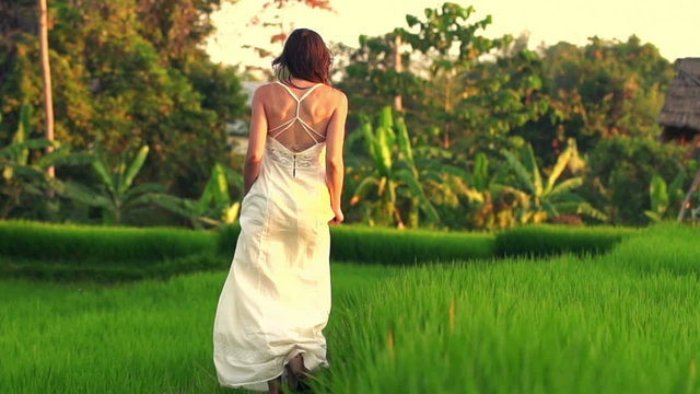 Woman in white dress walking through rice field, slow motion