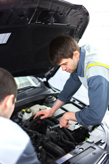 Fototapeta na wymiar Two auto mechanics examining car with open hood