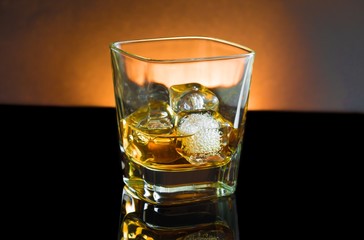 whiskey glass with ice and warm light on black background