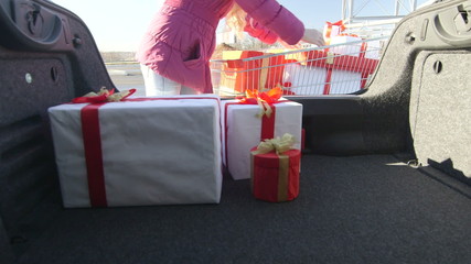Shopper with shopping cart full of gift boxes loads car trunk - Powered by Adobe