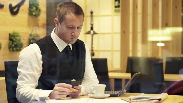 Businessman comparing data on smartphone, documents and laptop