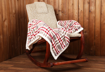 Rocking chair covered with plaid on wooden wall background