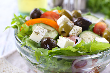 Greek salad in glass dish on napkin and wooden table background