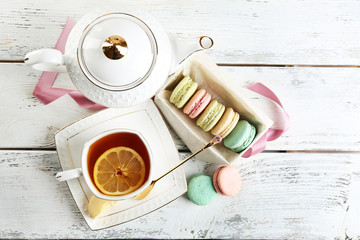 Colorful macaroons with cup of tea on wooden background