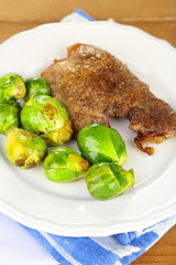 Roasted meat and vegetables on plate, on wooden table