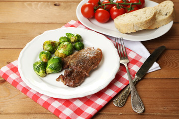 Roasted meat and vegetables on plate, on wooden table
