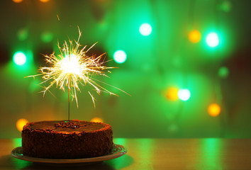 Tasty cake with sparkler on shiny background