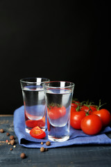 Glasses of ouzo and tomatoes on wooden table, on grey
