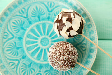 Tasty cake pops on plate, on wooden table