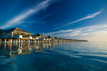 Over water villas in Maldives reflected in blue lagoon