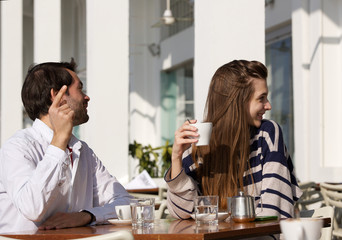 young couple sitting at outdoor cafe asking for the bill