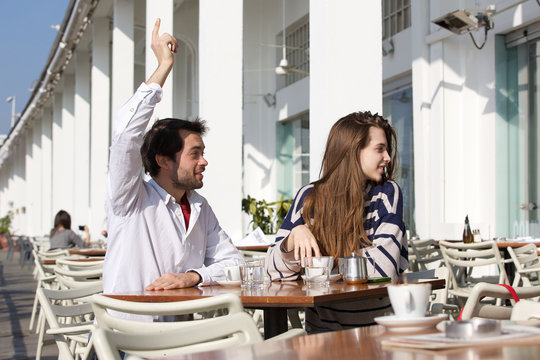 Man sitting at outdoor cafe with raised arm asking for waiter