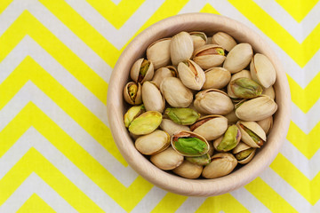 Pistachio nuts in wooden bowl on yellow and white cloth
