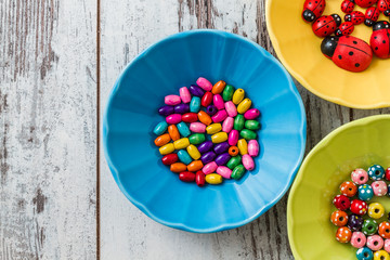 Multi Colored Beads and ladybirds on Colorful Small Plates on White Wooden Background