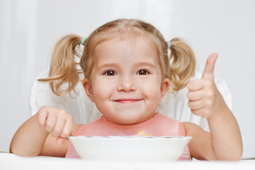 happy little girl eats with a spoon while sitting at table