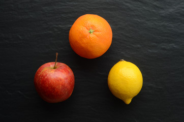 Top view of an apple, orange and lemon on a dark background