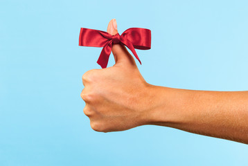 Hand making thumb up with red ribbon. Merry Christmas concept.