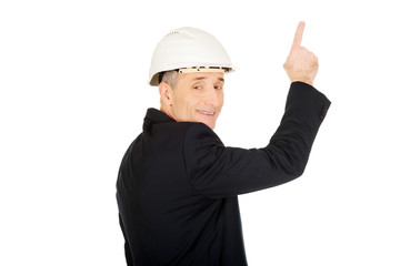 Smiling businessman with hard hat pointing up
