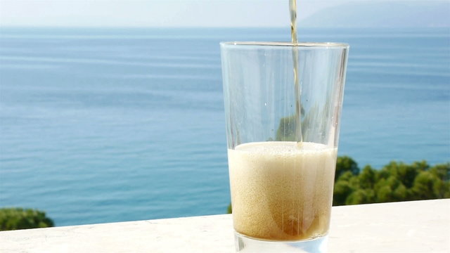 Pouring dark beer in glass with blue sea background