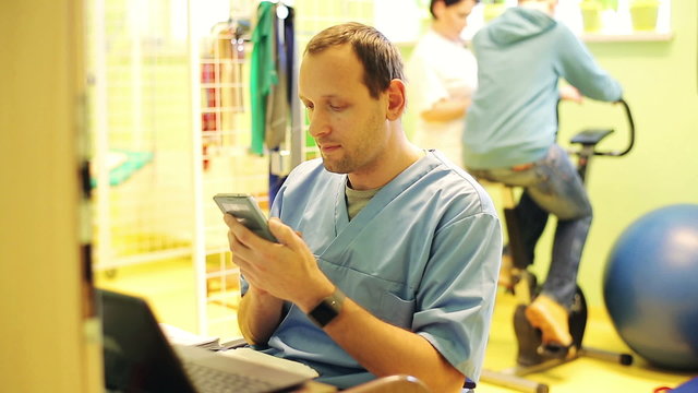 male doctor sitting  with smartphone in rehabilitation room
