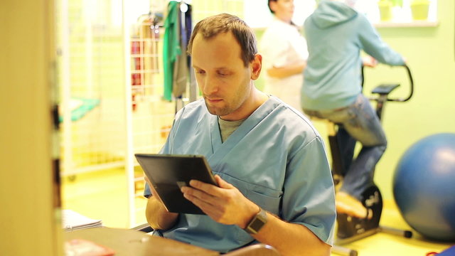 Young, male doctor with tablet computer in rehabilitation room