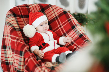 child dressed as Santa Claus sits in a plaid chair
