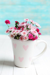 Beautiful flowers in cup on table on light blue background