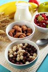 Various sweet cereals in ceramic bowls, fruits and jug with