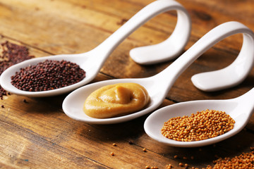 Mustard seeds, powder and sauce in spoons on wooden background