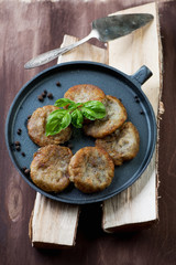 Frying pan with potato pancakes on wooden logs, vertical shot