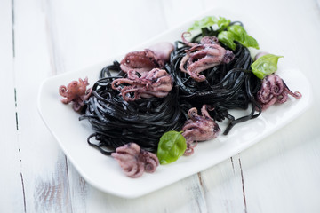 Black tagliatelle, octopuses and green basil, close-up