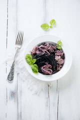 Black tagliatelle with octopuses and green basil, above view