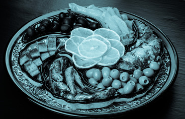 Assorty of fish, olives, lemon slices on oriental dish. Toned