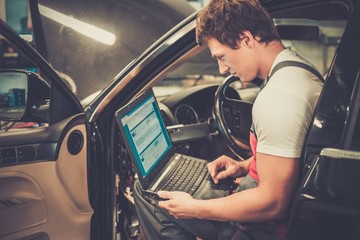 Serviceman making car diagnostics with laptop in a workshop