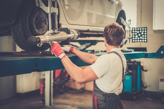 Young serviceman checking wheel alignment  in a car workshop