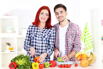 Happy couple cut vegetables in kitchen