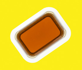 Maple syrup in a plastic container on a yellow background