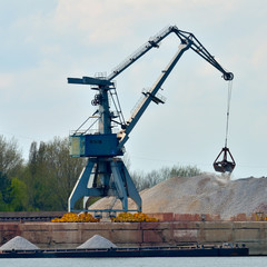 Crane loading industrial cargo ship with gravel