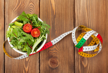 Tape measure and healthy food over wooden table