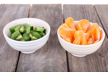 Bowls of slices kiwi and mandarin on rustic wooden background